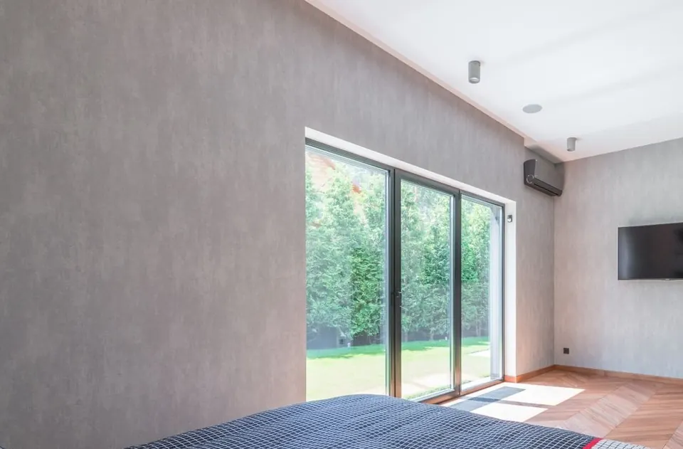 Ventanal corredero de aluminio gris antracita de tres hojas en un dormitorio, con un seto al otro lado
