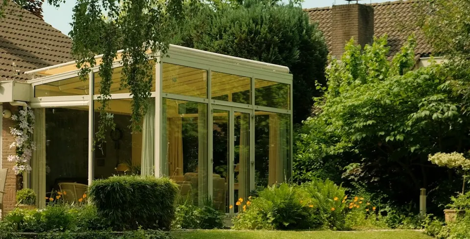 Cerramiento de aluminio blanco y vidrio con techo, adosado a una casa con jardín