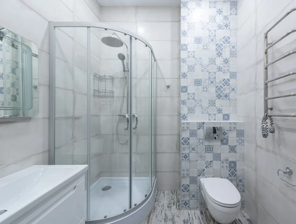 Mampara de ducha curva de vidrio con perfil de aluminio en un baño pequeño