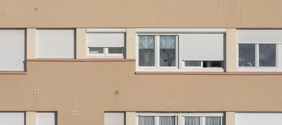 Fachada de un bloque de pisos con persianas enrollables blancas a distintas alturas