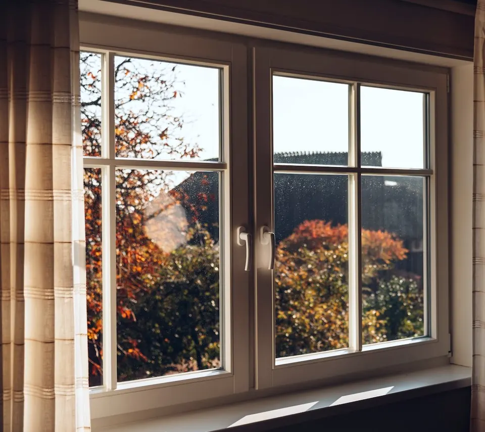Ventana blanca de dos hojas con sus manillas, vista desde dentro de una habitación