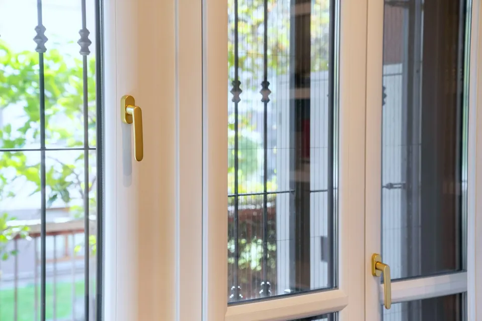Perfiles de una ventana de PVC con su manilla, y una reja de forja al otro lado del cristal